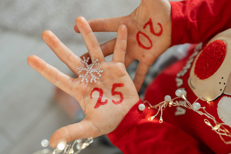 The numbers of the new year 2025 are written in red on children's palms. a child in a festive red...
