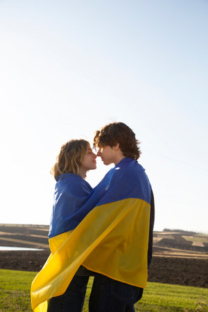 young couple in love, adult guy and girl, standing opposite each other, touching their noses one to one, wrapped in flag of Ukraine. Independence Day. Concept of love and patriotism. stop the warの写真素材