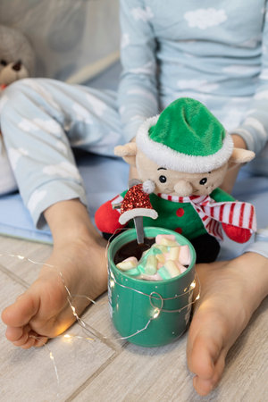 Close-up of a child's bare feet, a toy elf, and a cup of cocoa with marshmallows. winter weekends and holidays. Delicious children's drinks. Lifestyleの写真素材