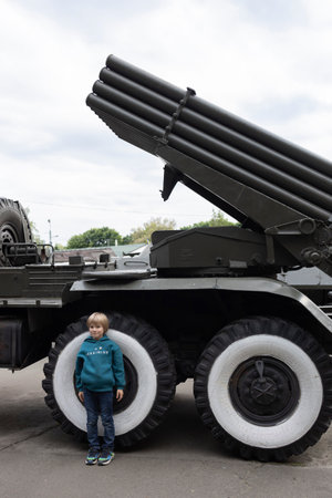 young boy stands near military vehicle, multiple launch rocket system. Russian invasion of Ukrainian...