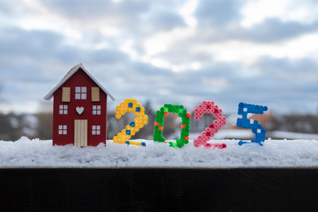 Happy New Year 2025 - numbers in the snow and a souvenir wooden figurine of a cozy home. postcard of winter festive mood for the change of year. home sweet home conceptの写真素材