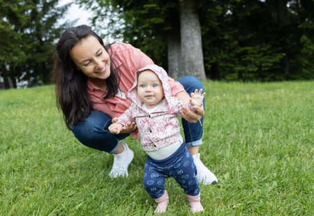 Portrait of a mother and child taking first steps. happy mother holding the hands of her little daughter walking along the green grass in the park. Lifestyle. The happiness of motherhoodの写真素材