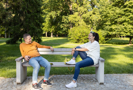 beautiful stylish couple in love is sitting on a bench in a city park. happily communicating and relaxing outdoors. Happy love and marriage concept.の写真素材
