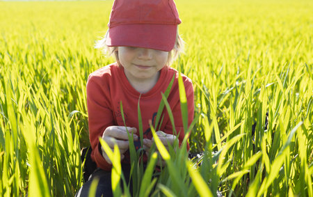 Portrait of a happy child in a red cap sitting on a green meadow on a bright sunny day. Rest and...