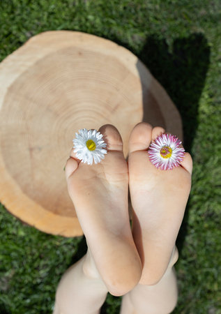 positive atmosphere, hello summer. Bare feet of a child and two daisy flowers between his toes on a...