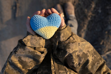Ukrainian soldier holds a knitted yellow and blue heart in hands. Stand with Ukraine. Day of...