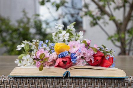 thick old open book lies on the table, on it is a bouquet of many different spring flowers. Read the...