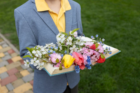 bouquet of beautiful various spring flowers lies on an open book in the hands of child. Cozy poetic aesthetic atmosphere. gift for mom on Mother's Day. flower fantasy. international book giving dayの写真素材