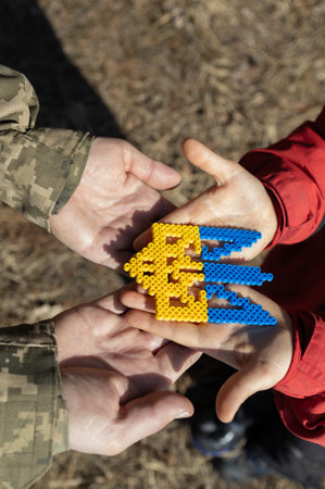 yellow-blue trident - national symbol of Ukraine - in hands of a child and an adult in an army...