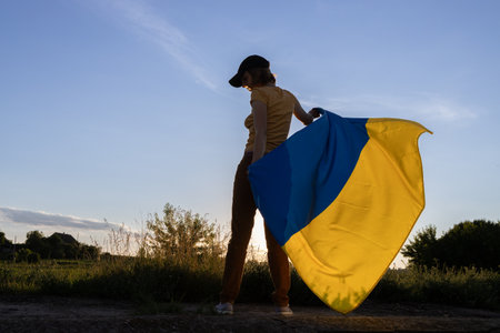 A woman holds a large Ukrainian yellow and blue flag behind her against a sunset sky. I am proud to be Ukrainian, a national symbol of freedom. Stand with Ukraineの写真素材