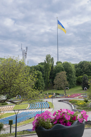 A large Ukrainian flag flutters against a cloudy sky and the Motherland statue. Kyiv landmark for tourist visitsの写真素材