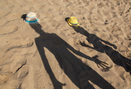 Shadow of two people, an adult and a child, on the sand in bright sunlight. Interesting shadows. People are fooling around and having fun while relaxing on the sandy coastの写真素材