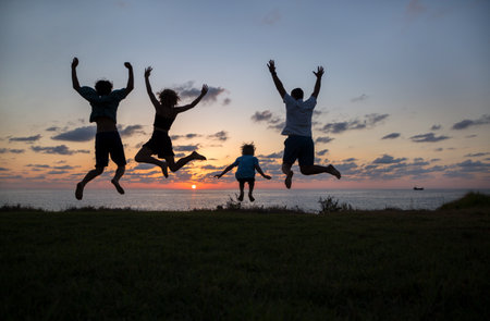 silhouette of 4 people jumping up and down joyfully, having fun at sunset by the sea