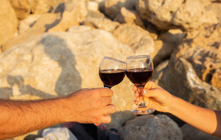 Glass goblets with red wine in hands of two people against background of a rock illuminated by the sunの写真素材