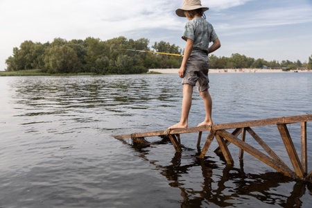 barefoot child, boy 8 years old, enthusiastically catches fish on a lake or river. Healthy...