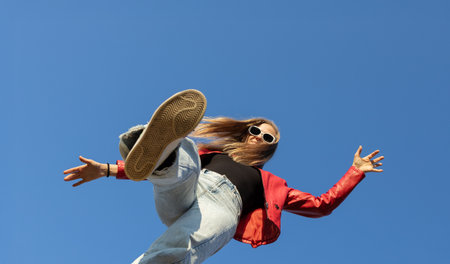 Dynamic low angle shot of a young woman boldly stepping forward against a clear blue sky. vitality, freedom and joy, motivation to move. copy space.の写真素材