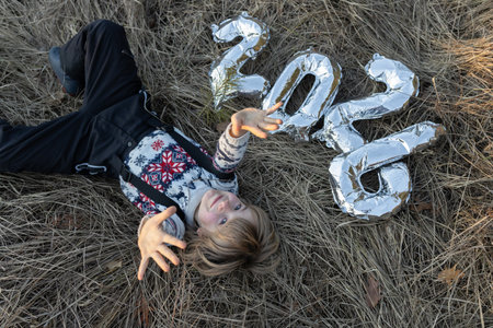 A happy child, an 8-year-old boy in a Christmas sweater, lies on dry, snow-free grass, and the...
