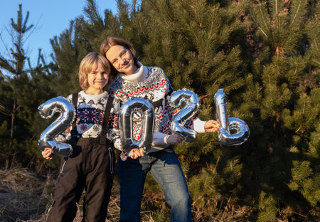 happy family: mother and son in New Year's sweaters holding balloons with the numbers 2026. Concept...