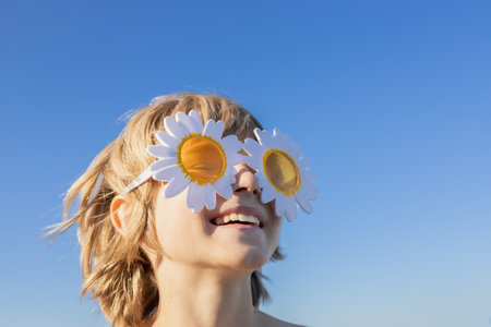 cheerful portrait of a happy child on a sunny day against blue sky. A sincere smile, daisy-shaped glasses, and an atmosphere of joy and childish happinessの写真素材