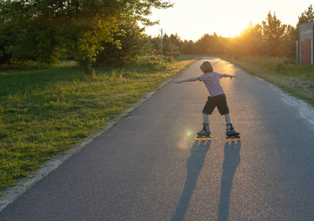 boy roller skates at sunset on a sunny summer evening, making long shadows. Happy childhood. Active...
