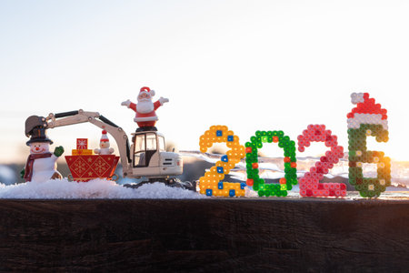 toy excavator with the numbers 2026, souvenir Santa and snowman figurines in the snowの写真素材