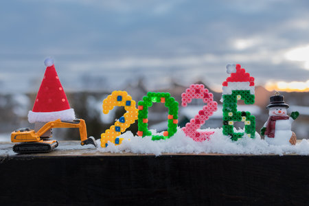 funny photo of a toy excavator with a Santa hat, a festive souvenir snowman, and the numbers 2026 in...