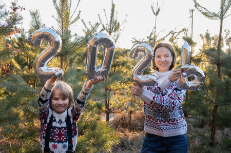 happy, cheerful family: mother and son in New Year's sweaters holding balloons shaped like numbers...