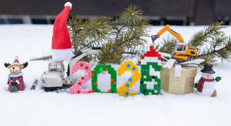 composition of toy excavator models, Christmas souvenirs, and the numbers 2026 in the snow. A...