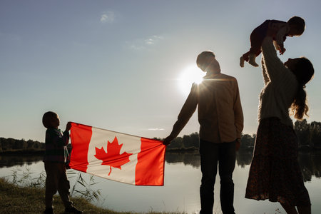 young happy family, parents with two children, holding a large Canadian flagの写真素材