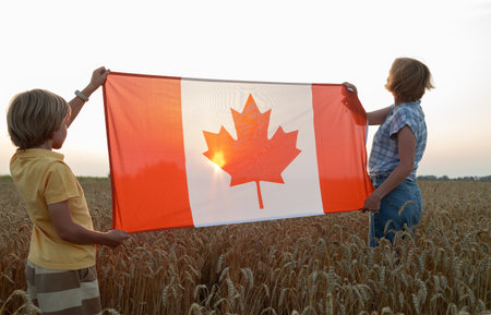woman and child, mother and son, hold a large Canadian flag standing in a wheat field at sunset. Happy Canada Day, freedom, patriotism. Traveling the countryの写真素材