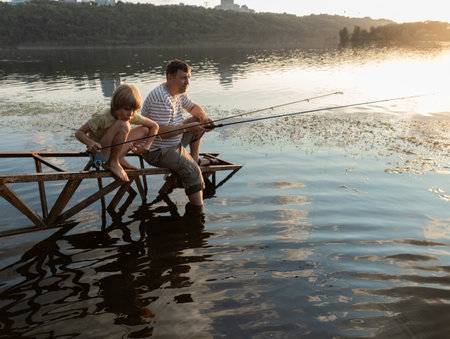 father and son fish together on a sunny summer day, holding fishing rods and waiting for a bite. Space for text. Family Hobbies.の写真素材