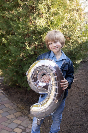 Happy Birthday. Portrait of a happy, sweet 9-year-old boy holding a silver balloon in the shape of...