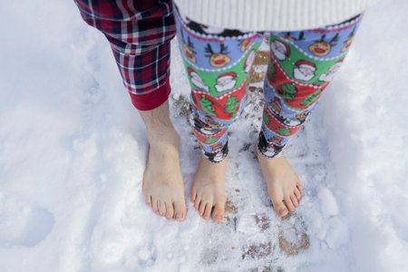 bare feet of adult man and child in pajamas, standing next to each other barefoot in freshly fallen snowの写真素材