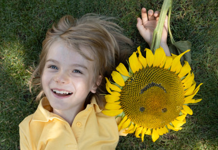 cute boy's face next to a sunflower with a carved smile. Summer mood, floral fantasies, positive vibes. Hello, summer Positive child. Happy childhood.の写真素材
