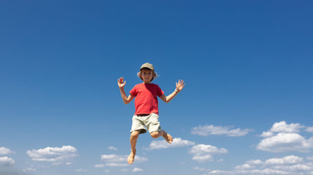barefoot boy joyfully jumps against a blue sky. Concept of freedom and happiness. Energy, active youth, healthy lifestyle, delight, inspiration. Vitality and joy, motivation to move. Space for text.の写真素材