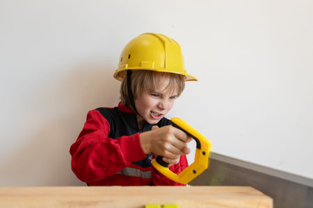 little construction worker in a yellow hard hat diligently saws. A child dressed in a construction...