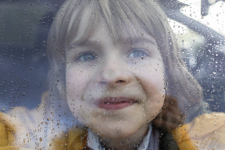 happy boy pressed his nose to the window of a car, covered with drops from the rain. Changeable...