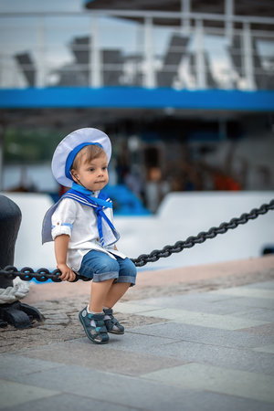 a boy dressed as a sailor sits on the pier, looks at the ships and dreamsの写真素材