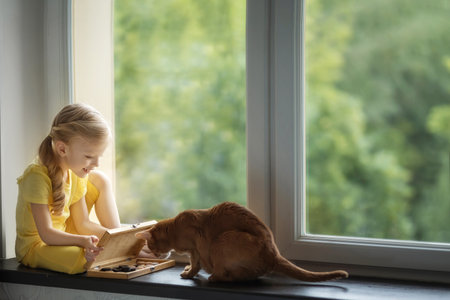 Beautiful girl on the windowsill plays checkers with a catの写真素材