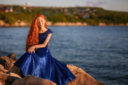beautiful romantic girl with red hair greets the sunrise on the seashoreの写真素材