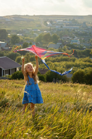 In summer, a girl is flying a kite on the field. Plays outdoors in the park at sunset. The child plays in nature.の写真素材