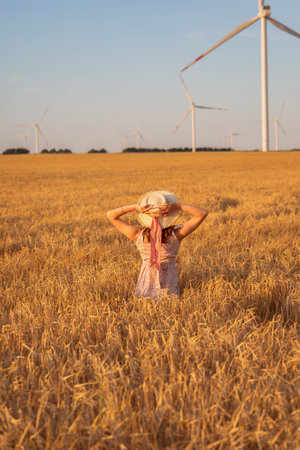 Beautiful girl at sunset in a wheat field with windmills to generate electricity. The concept of renewable energy, love for nature, electricity. Renewable energy.の写真素材