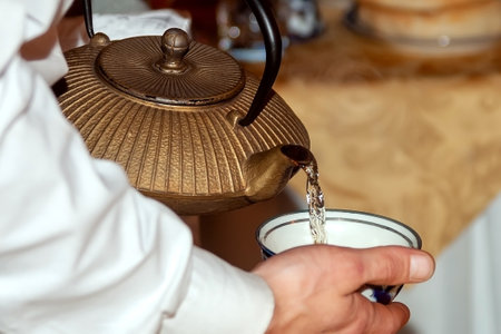 Close-up of a man's hand pouring tea from a teapot into a bowl for tea ceremonyの写真素材