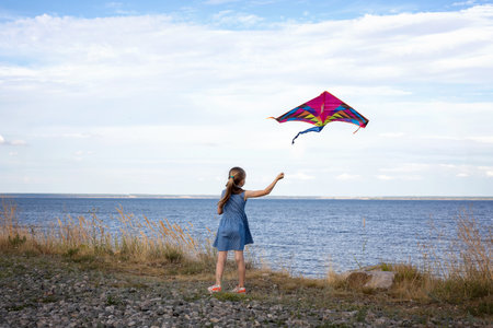 little  beautiful girl playing with flying kite on the coast. Kite flying in the wind. The child plays outdoors in the beach.の写真素材