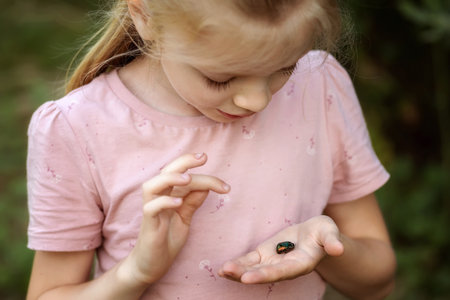 A little girl examines a beetle on her hand. A child studies nature.