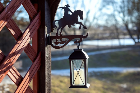 Black metal lantern with a cowboy on horseback silhouette, attached to a wooden structure, with a blurred natural background. Rustic outdoor decorの写真素材