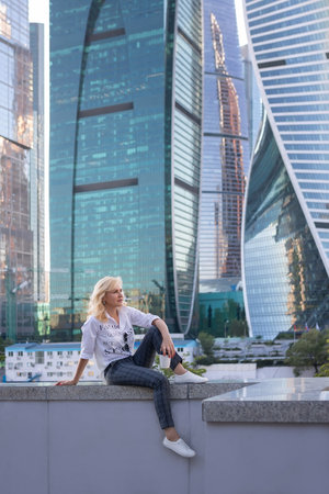 blonde woman resting with a cup of coffee on the background of skyscrapersの写真素材