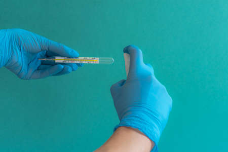 Women's hands in gloves with a thermometer, hands in gloves, women's hands, blue medical gloves,...