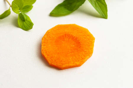 A sprig of mint and a carrot on a white background. Vitamin kit. Ingredients for carrot juice with mint. Isolated carrots and mint. Food preparation. Products on a white background in sunlight.の写真素材