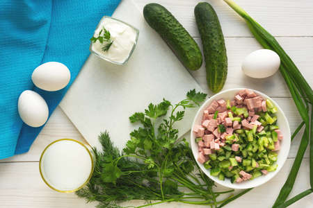 Ingredients for the traditional Russian cold soup okroshka. Sliced foods. The view from the top. Food preparation. Cucumbers, eggs, dill, onions, sour cream and kefir on a white wooden background.の写真素材